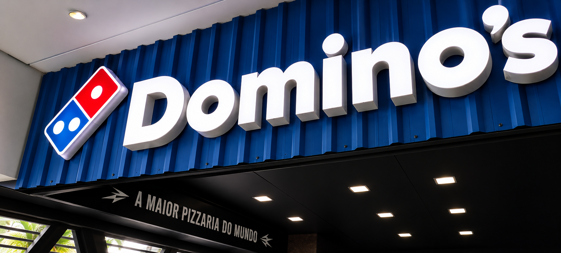 Letreiro luminoso Dominos em fachada azul com letras caixa iluminadas